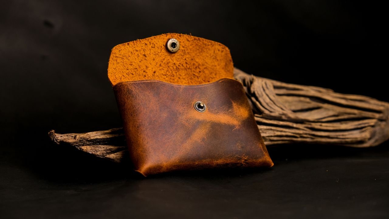 Close-up of a handcrafted leather coin purse displayed on driftwood, showcasing artisan skills.